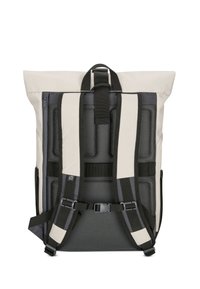 Sac à dos beige au design à rabat, avec panneau arrière en mesh noir, bretelles rembourrées et hardware réglable. Tissu résistant et forme moderne.