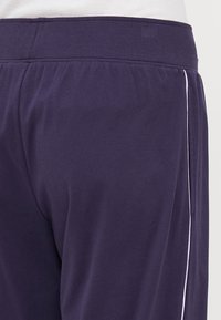 Mörklila sportbyxor med elastisk midja, med vita sidestreck och en mjuk, slät textur.