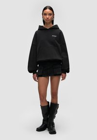 Czarna, oversize bluza z kapturem, z kieszenią z przodu i logo, w połączeniu z krótką, czarną spódnicą dżinsową z kieszeniami cargo, uzupełnioną o czarne kozaki do kolan.