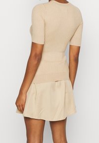 Beige ribbad kortärmad topp med en figursydd design, tillsammans med en ljusbeige utsvängd minikjol. Mjuk textur och slätt tyg.