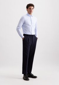 Camicia a maniche lunghe a righe blu chiaro e bianche, abbinata a pantaloni a pieghe blu scuro e scarpe eleganti nere. Vestibilità su misura con design classico.