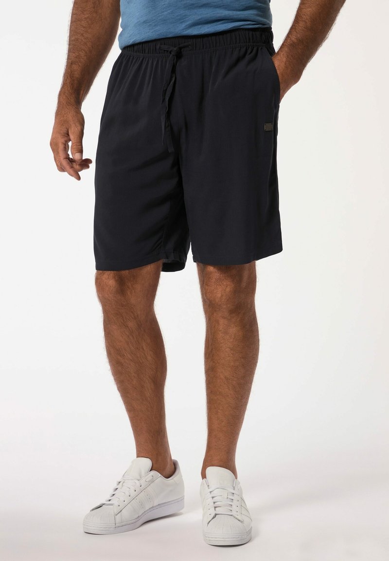 Costume da bagno blu navy con vita elasticizzata e coulisse, dotato di tasche laterali e una texture liscia. Indossato con sneakers bianche.