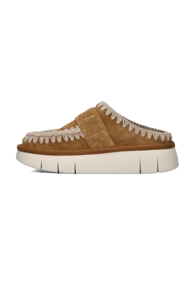 Chaussure slip-on en daim marron avec une épaisse semelle blanche, dotée d'accents tissés le long du bord supérieur et d'une large lanière sur le pied.