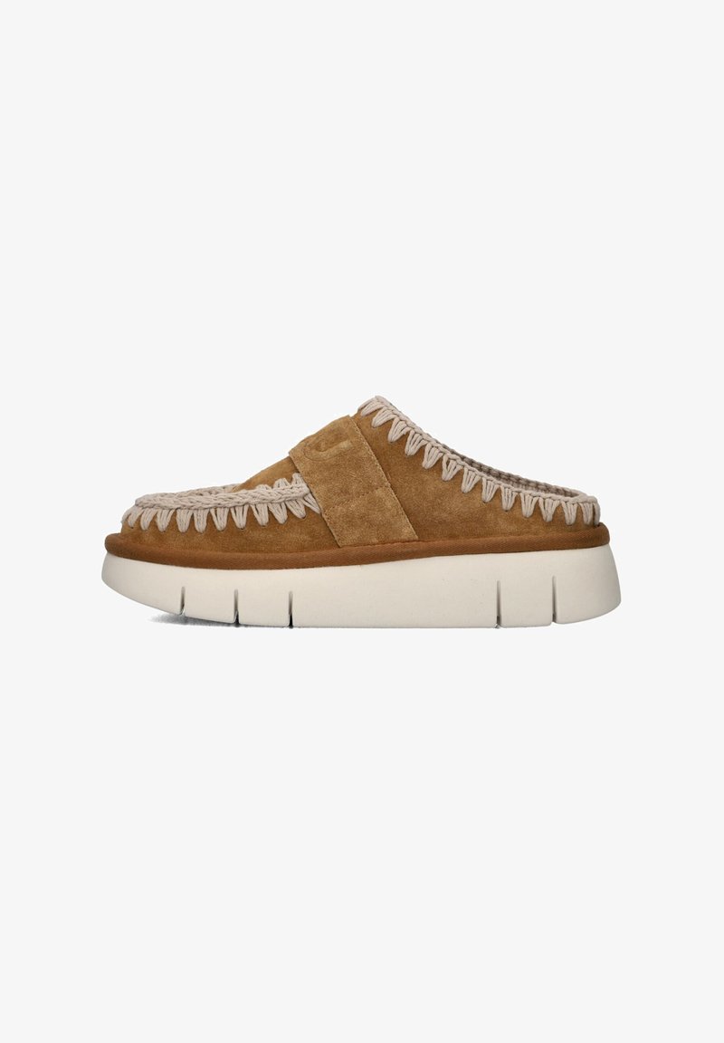 Chaussure slip-on en daim marron avec une épaisse semelle blanche, dotée d'accents tissés le long du bord supérieur et d'une large lanière sur le pied.