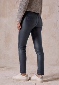 Mörkblå skinny jeans med en slät textur, bakfickor och en slim fit. I kombination med vita sneakers med grå detaljer.