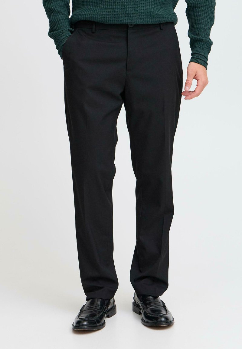 Μαύρο παντελόνι με ίσια γραμμή, κατασκευασμένο από λεία υφή. Διαθέτει μπροστινές τσέπες και φερμουάρ, συνδυασμένο με μαύρα παπούτσια.