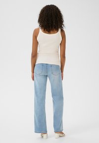 Helles beiges geripptes Tanktop kombiniert mit hellblauen Schlagjeans. Die Jeans haben Gesäßtaschen und einen lässigen Schnitt. Neutrale Schuhe runden den Look ab.