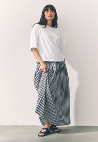 Camicia bianca a maniche corte abbinata a una lunga gonna arricciata a quadretti bianchi e neri. Calzature con sandali neri con fiocchi.