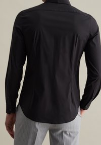 Schwarzes Langarmhemd mit glatter Textur, spitzem Kragen, geknöpften Manschetten und geschwungenem Saum, kombiniert mit hellgrauen Nadelstreifenhosen.