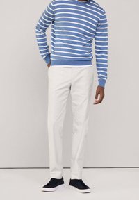 Modrý a bílý pruhovaný svetr z bavlněné směsi s kulatým výstřihem; doplněný bílými kalhotami a černými teniskami s bílými podrážkami.