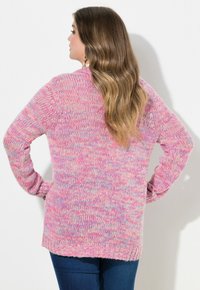 Stickad kofta i rosa med fläckar i flera färger, som har långa ärmar, en avslappnad passform och en ribbad nederkant. Texturen verkar mjuk och mysig.