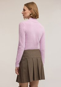 Jasnoróżowy, miękki golf połączony z brązową plisowaną spódnicą w kratę. Spódnica ma wysoki stan i teksturowany wzór.