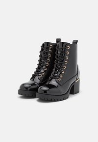 Czarne lakierowane botki za kostkę z złotymi oczkami, sznurówkami, masywnym obcasem oraz grubą, teksturowaną podeszwą. Zawierają pętelkę z tyłu.
