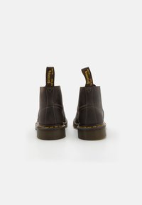 Brune lær ankle boots med gule sømmer, gummisål og bånd med tekst. Glatt tekstur og avrundet tådesign.