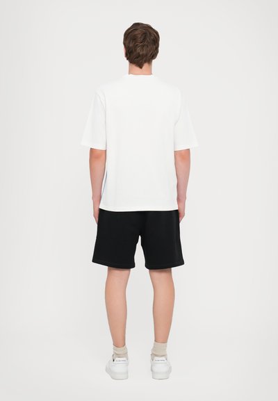 T-shirt en coton blanc à manches courtes et col rond, associé à un short noir. Le short a une texture unie et une coupe décontractée.