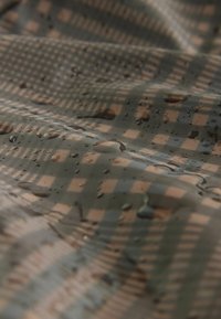 Tejido resistente al agua con un patrón de cuadros en verde y marrón, que presenta una textura suave y gotas en la superficie.