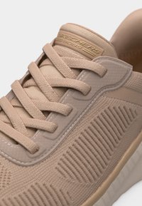 Ανοιχτό μπεζ αθλητικό παπούτσι Skechers με υφή πλεκτού υφάσματος, κορδόνια στο ίδιο χρώμα και γλώσσα με το λογότυπο "Skechers BOBS".