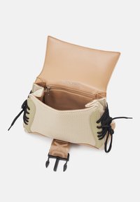 Bolso de cuero beige con exterior de malla y acentos verdes. El interior cuenta con un bolsillo con cremallera y una correa ajustable con herrajes para un cierre seguro.