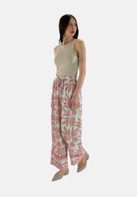 Beige mouwloos topje gecombineerd met losse, witte palazzo-broeken met roze bladranden. Gedragen met naakte hakken.