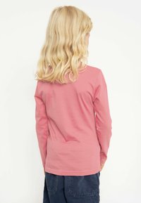 Langärmliges Shirt aus weichem, rosa Baumwollstoff mit Rundhalsausschnitt, das eine glatte Textur und einen leicht lockeren Schnitt aufweist, kombiniert mit marineblauen Shorts.