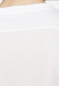 Biała koszulka sportowa z gładkiego materiału na górze oraz siateczkowym, perforowanym wzorem na dole, zapewniającym wentylację. Prosty design, bez wzorów.