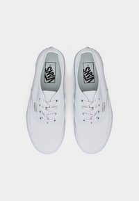 Baskets Vans blanches à tige basse avec lacets blancs, vues de dessus sur un fond uni.