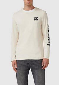 Crème lange mouw t-shirt van katoen met een ronde hals, voorzien van een zwart logo op de borst en "Discovery" in het zwart op de mouw gedrukt.