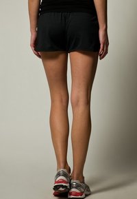 Shorts de sport noirs à coupe décontractée, accompagnés de chaussures de course grises et rouges. Accent sur les jambes et les chaussures ; arrière-plan minimaliste.