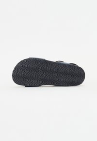 Svart såle til sandaler med et teksturert, bølgete mønster for bedre grep. Kantene er avrundede, og materialet ser slitesterkt og fleksibelt ut.