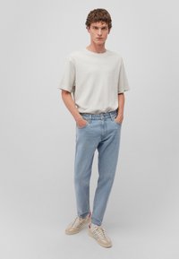 Hellgraues Baumwoll-T-Shirt kombiniert mit blauen Jeans. Modell trägt beigefarbene Sneakers mit Akzentstreifen. Einfaches Design, lockere Passform.