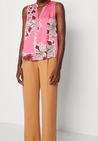 Rosa ärmlös blus med blommönster, med en framficka och lös passform, parat med beige vida byxor. Slät tygkänsla.