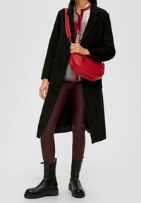 Abrigo negro, bolso rojo, camisa de cuadros y pantalones burdeos. Botas negras gruesas con un acabado texturizado, que presentan un diseño de suela distintivo.