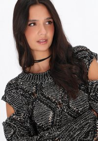 Maglione lavorato a maglia bianco e nero con design a spalla scoperta, caratterizzato da un motivo testurizzato e colletto a girocollo a coste. Materiale morbido.