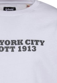 Biała bawełniana koszulka z wyraźnym czarnym napisem: "NEW YORK CITY SCHOTT 1913" w wyrazistej czcionce. Okrągły dekolt, teksturowana tkanina.