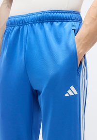 Μπλε αθλητικό παντελόνι από λεία ύφανση, με λευκές πλαϊνές ρίγες και μικρό λευκό λογότυπο στο μηρό. Η μέση έχει ελαστική ζώνη.