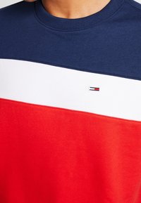 Färgsatt sweatshirt med sektioner i marinblått, vitt och rött. Ribbad krage och liten logotypdetalj nära mitten. Bomullsmaterial.