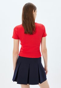 Top rojo de manga corta ajustado con textura acanalada, combinado con una falda de tablones azul marino. El conjunto enfatiza líneas limpias y una estética informal.
