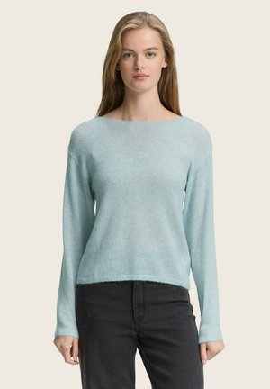 Pull bleu clair en tissu doux et texturé ; possède un large col et des manches longues, associé à un pantalon foncé.