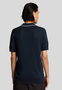 Polo shirt corto navy con una texture morbida, caratterizzato da un colletto bianco e orlo dritto. La vista posteriore mostra dettagli di design minimi.