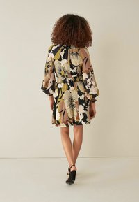 Robe fleurie avec des manches cloche, motif multicolore en beige, noir et olive. Taille cintrée avec ornement, longueur genou, tissu léger.