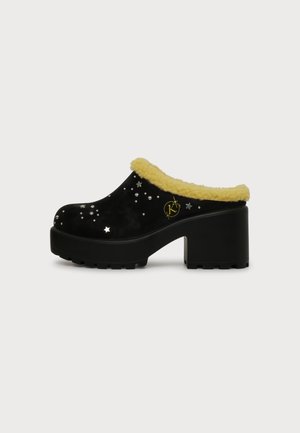 Sabot à plateforme noir avec talon épais, doublure en polaire jaune et ornements en forme d'étoile et de clous argentés sur le dessus.