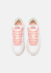 Zapatillas deportivas blancas y rosas con una textura de ante, acentos verdes en el talón y cordones de tela. Presenta un logo en la lengüeta.