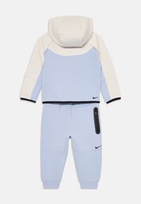 Šviesiai mėlynas džemperis ir kelnės su balta akcentu ant kapucės, juodu apvadu ir užtrauktuku ant kelnių kišenės. "Nike" logotipas abiejuose drabužiuose.