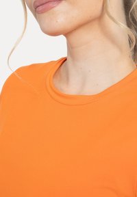 Camiseta naranja con cuello redondo, confeccionada en tela suave. Presenta un diseño sencillo, centrado en un color vibrante y líneas limpias.