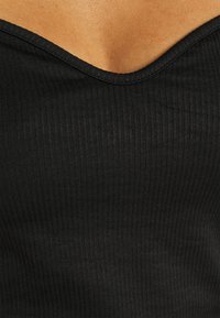 Svart ribbad linne med V-ringning. Tyget är mjukt med en lätt stretch och har strukturerade vertikala linjer.