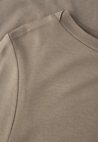Zwei überlappende beige Stoffabschnitte, die eine glatte Textur und ein klassisches Rundhalsdesign mit sorgfältigen Nähdetails zeigen.