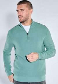 Hellgrüner Reißverschluss-Pullover mit strukturiertem Muster und langen Ärmeln, ausgestattet mit hohem Kragen und gerippten Bündchen.