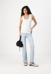 White ribbed tank top with lace trim, light blue flared jeans, and black patterned handbag. Beige shoes with pointed tips and straps.