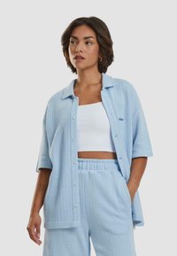 Light blue knit shirt with short sleeves and button closure, paired with matching knit pants. Features a textured pattern and relaxed fit.