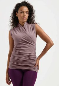 Haut sans manches violet avec un design enroulé et une texture froncée, fabriqué en doux tissu. Associé à des leggings violets.